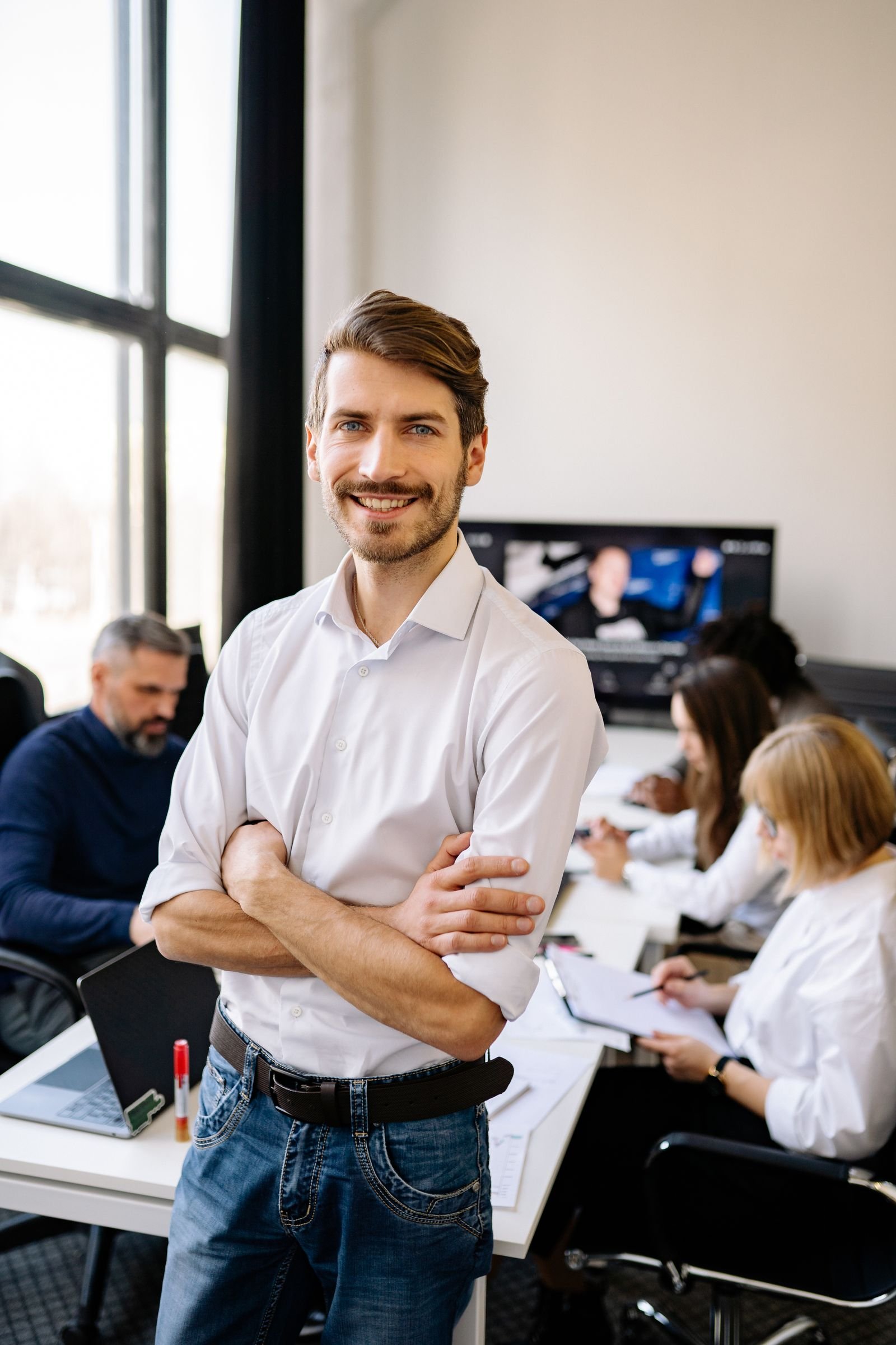Lächelnder Mann im weißen Hemd im Büro, Team im Hintergrund