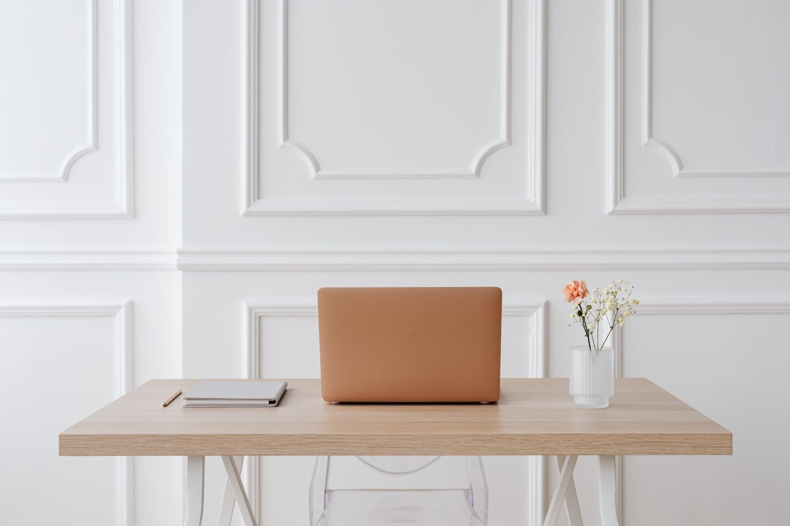 Aufgeräumter Schreibtisch mit Laptop und Notizbuch vor heller Wand