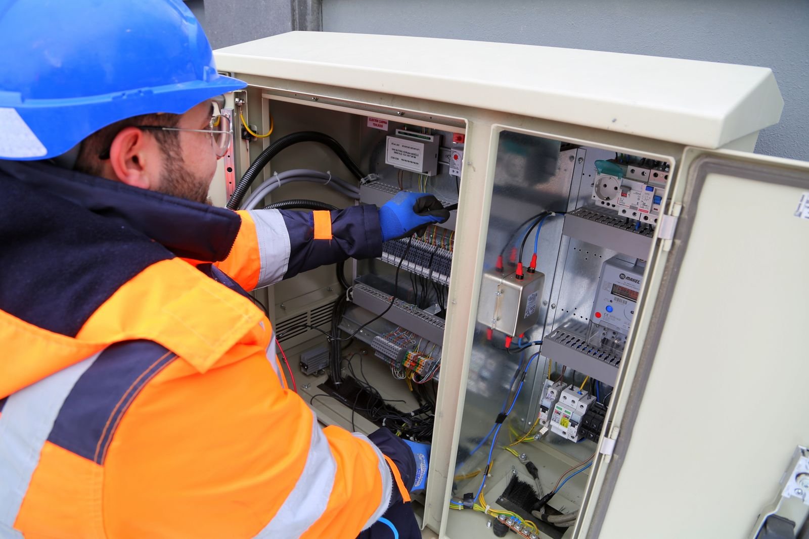 Elektriker mit Helm arbeitet an einem geöffneten Schaltschrank