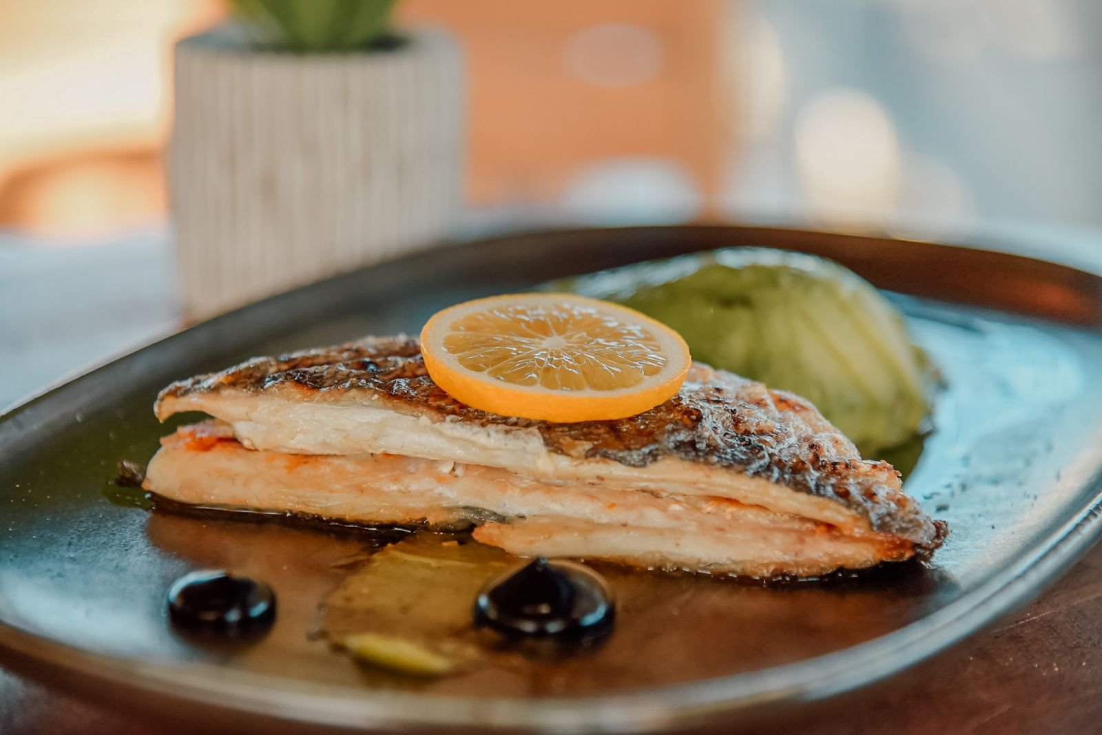 Gebratenes Fischfilet mit Zitrone, angerichtet auf dunklem Teller