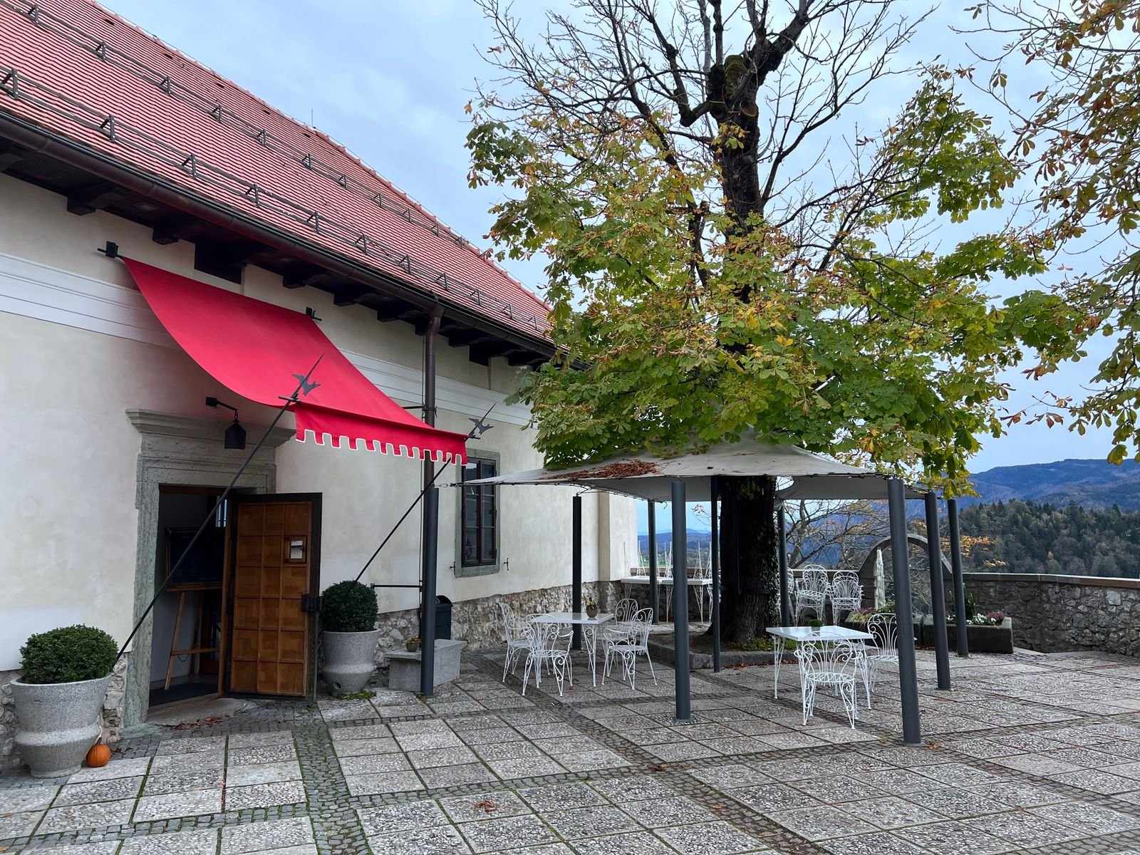 Gastgarten unter alten Bäumen vor einem traditionellen Gasthaus mit roter Markise
