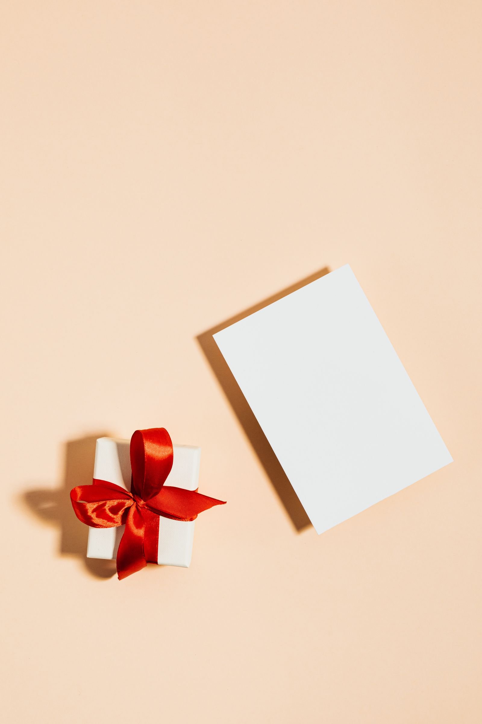 Kleines Geschenk mit roter Schleife und leerer Karte auf hellem Hintergrund