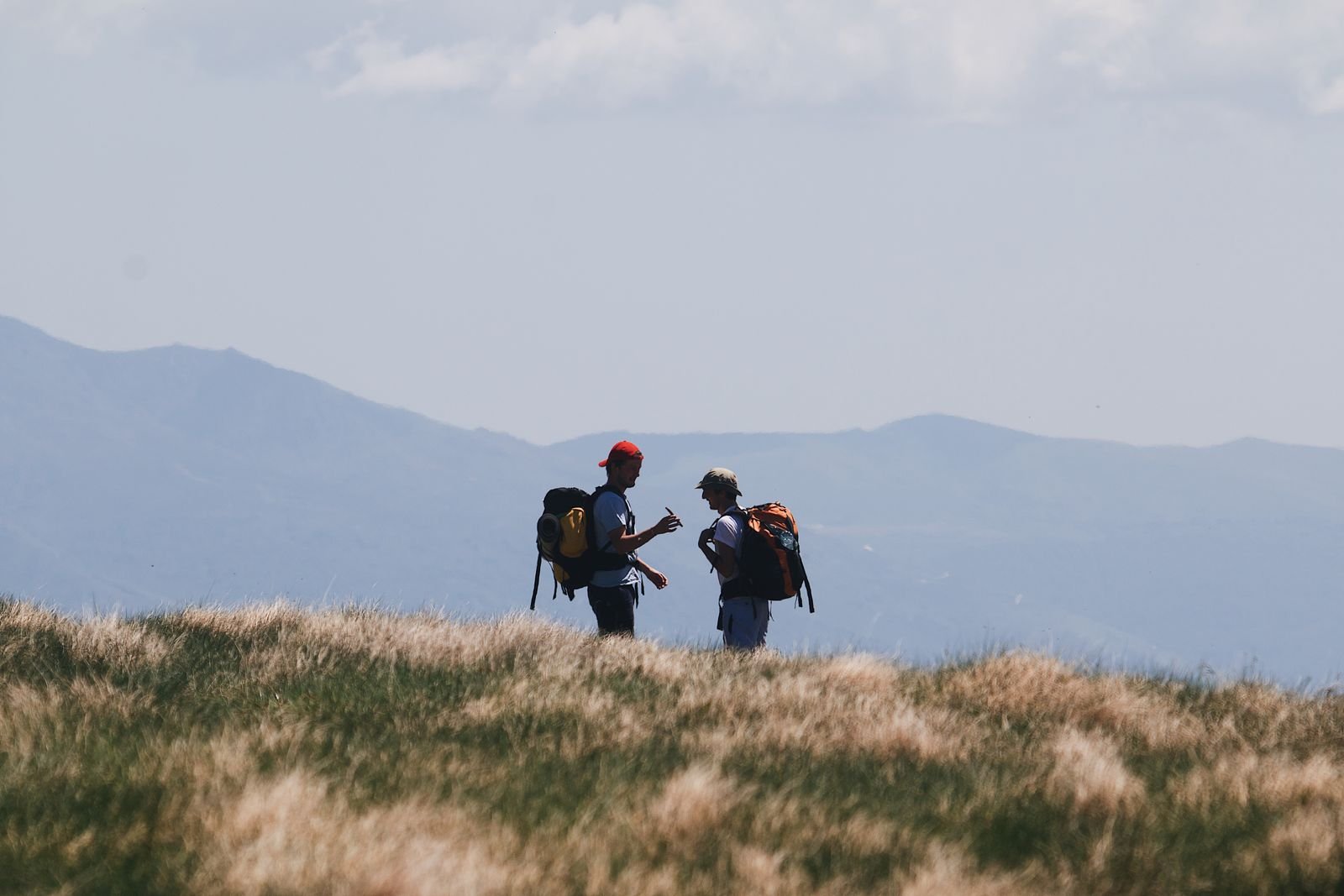 Zwei Wanderer mit Rucksack auf einer Almwiese vor Bergkulisse